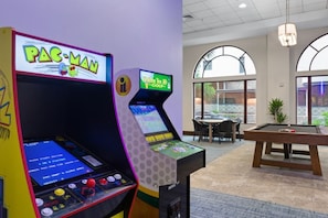 Une pièce équipée de deux bornes d’arcade, d’une table de billard et de grandes fenêtres en arc de cercle.