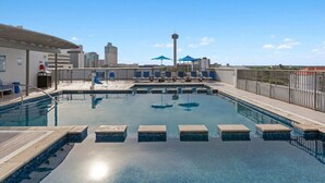 A rooftop swimming pool with lounge chairs and umbrellas, surrounded by a metal fence and city buildings in the background. - Wyndham La Cascada, San Antonio 1 Bedroom Condo (San Antonio)