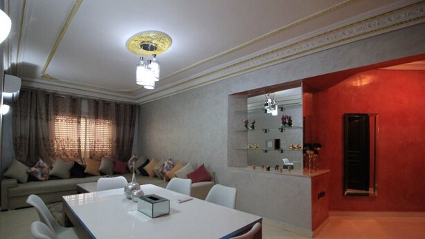 Uma sala de estar moderna com área de jantar, um conjunto de sofás, uma mesa de centro e uma parede de destaque vermelha.