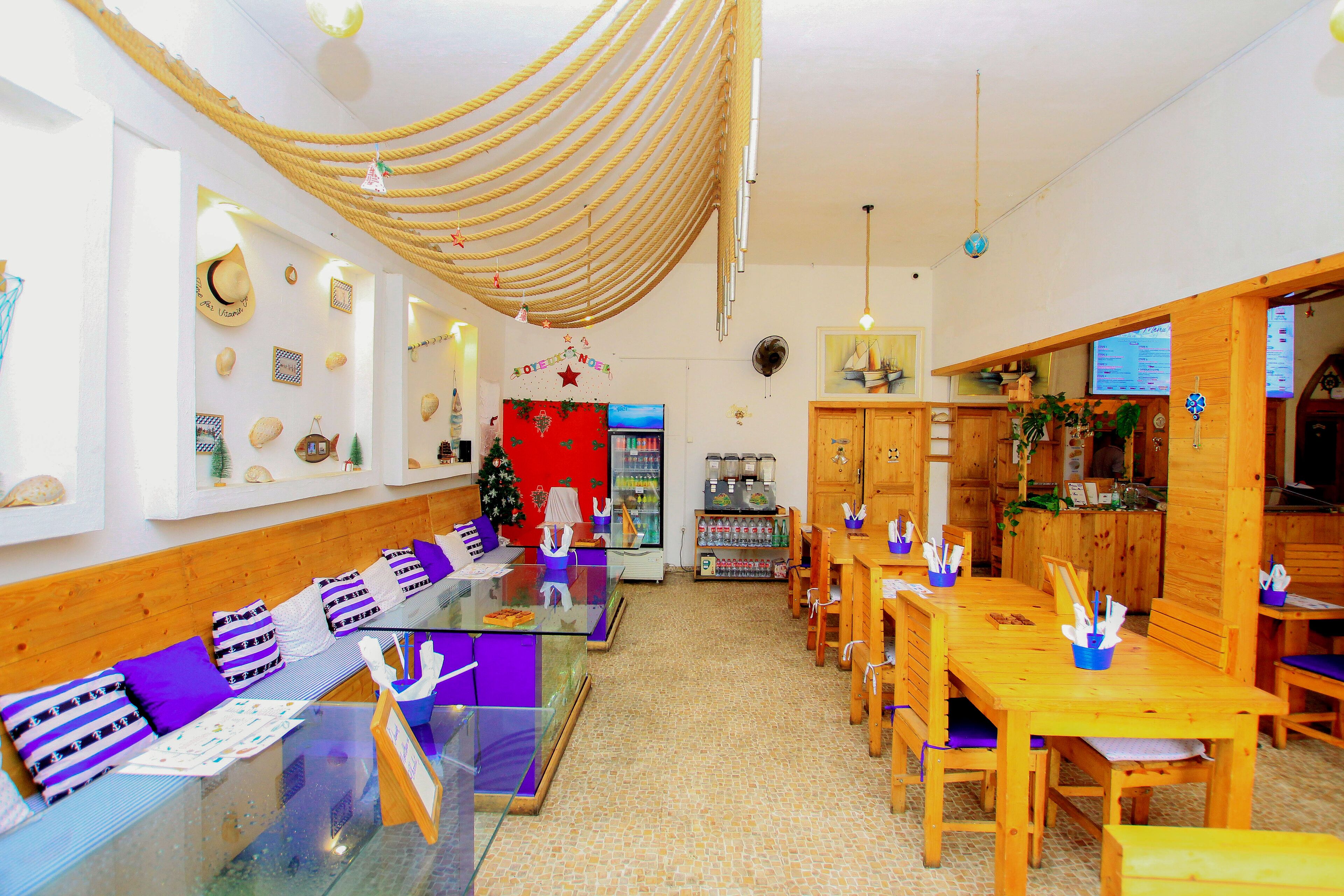 Un restaurante con una barra larga, mesas y sillas de madera. Se ve un árbol de Navidad y un panel con el menú.
