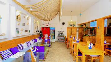 Un restaurante con una barra larga, mesas y sillas de madera. Se ve un árbol de Navidad y un panel con el menú.