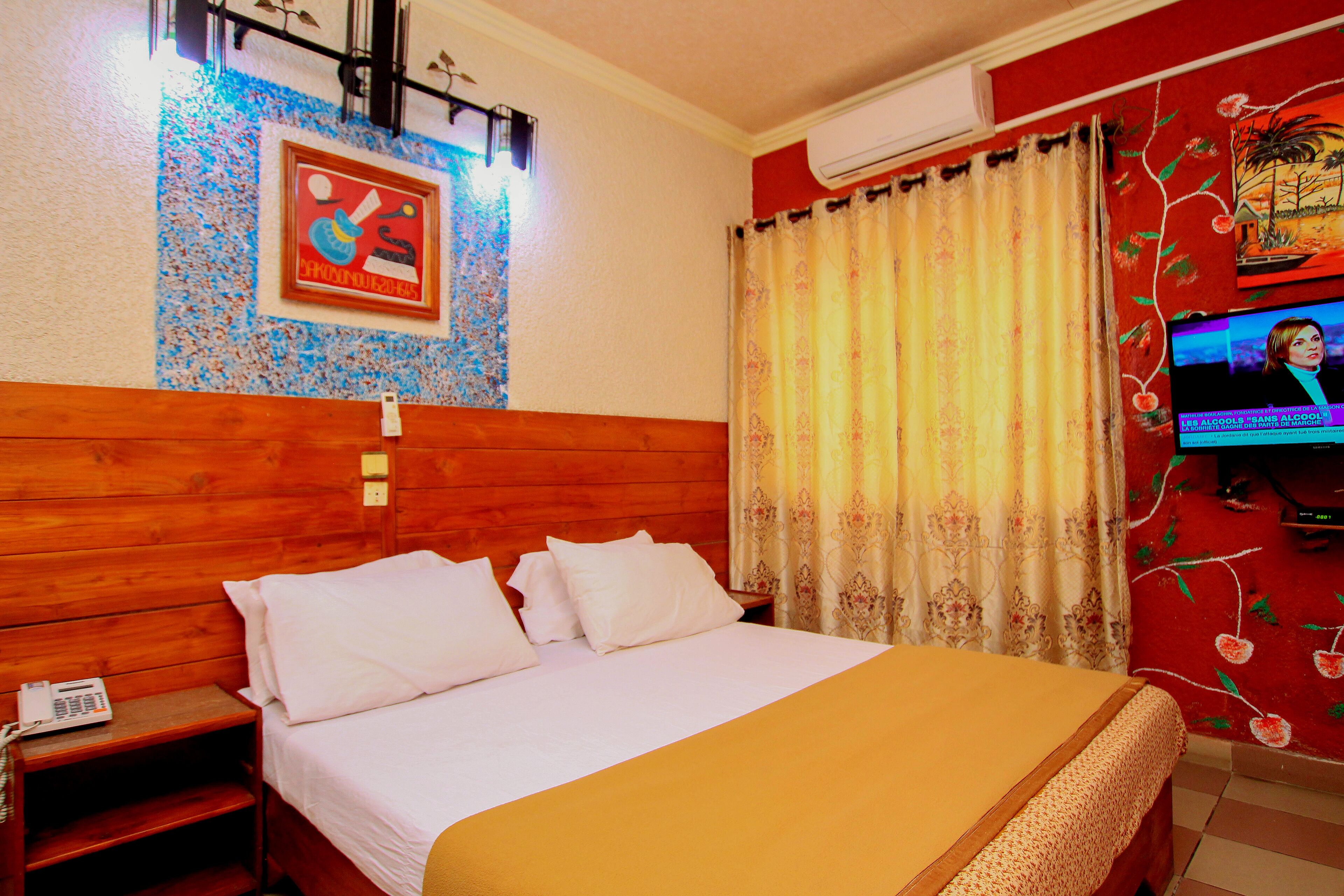 Habitación de hotel con cabecera de madera, cama con ropa blanca, mesita de noche con teléfono y televisor en la pared.