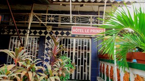Ein Hotel Eingang mit einem Schild, das "Hôtel Le Prince" zeigt, umgeben von Topfpflanzen und einem dekorativen Zaun.