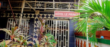 Entrada de un hotel con un cartel que dice "Hôtel Le Prince", rodeada de plantas en macetas y una valla decorativa.
