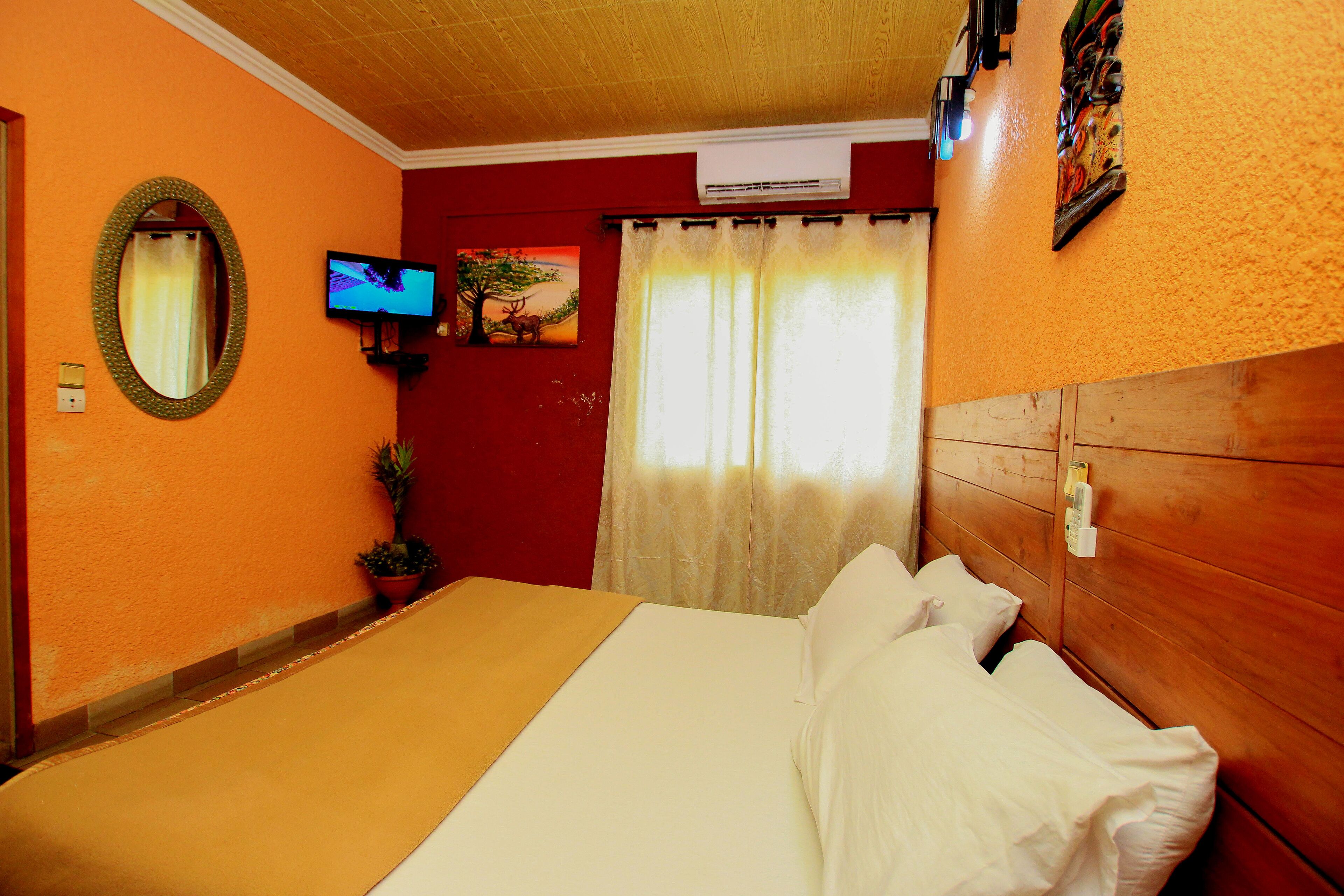 Habitación de hotel con cama, televisión, espejo y ventana con cortinas.