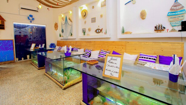 Ein Zimmer mit Glastauslagen, die verschiedene Gegenstände zeigen, einem hölzernen Bettvorhang und Wanddekorationen, darunter ein Schiff und Muscheln.
