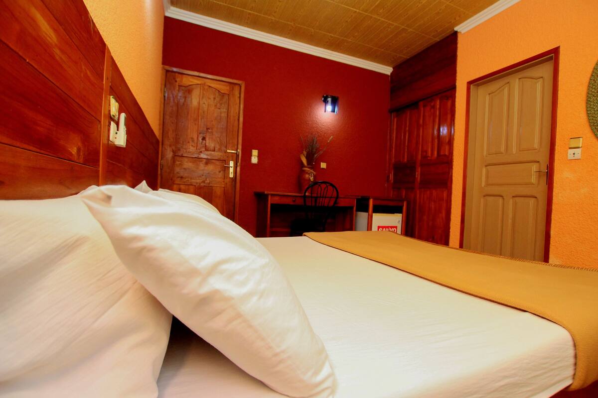 A room with a bed, wooden walls, and a red accent wall.