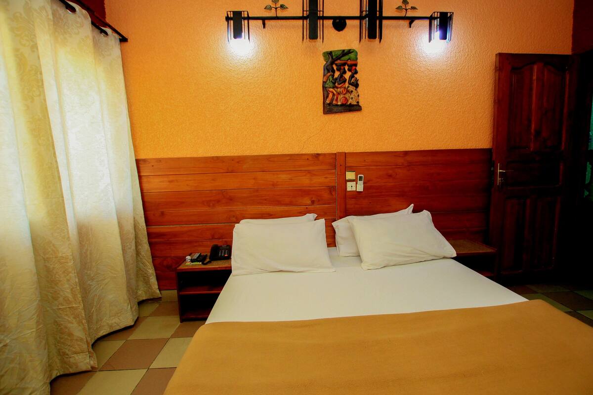 A hotel room with a wooden headboard, a bed with white linens, a nightstand with a phone, and a wall-mounted light fixture.
