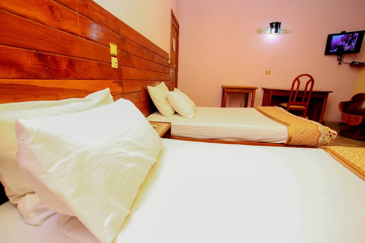 A hotel room with two beds, a wooden headboard, a television on the wall, and a small desk with a chair.