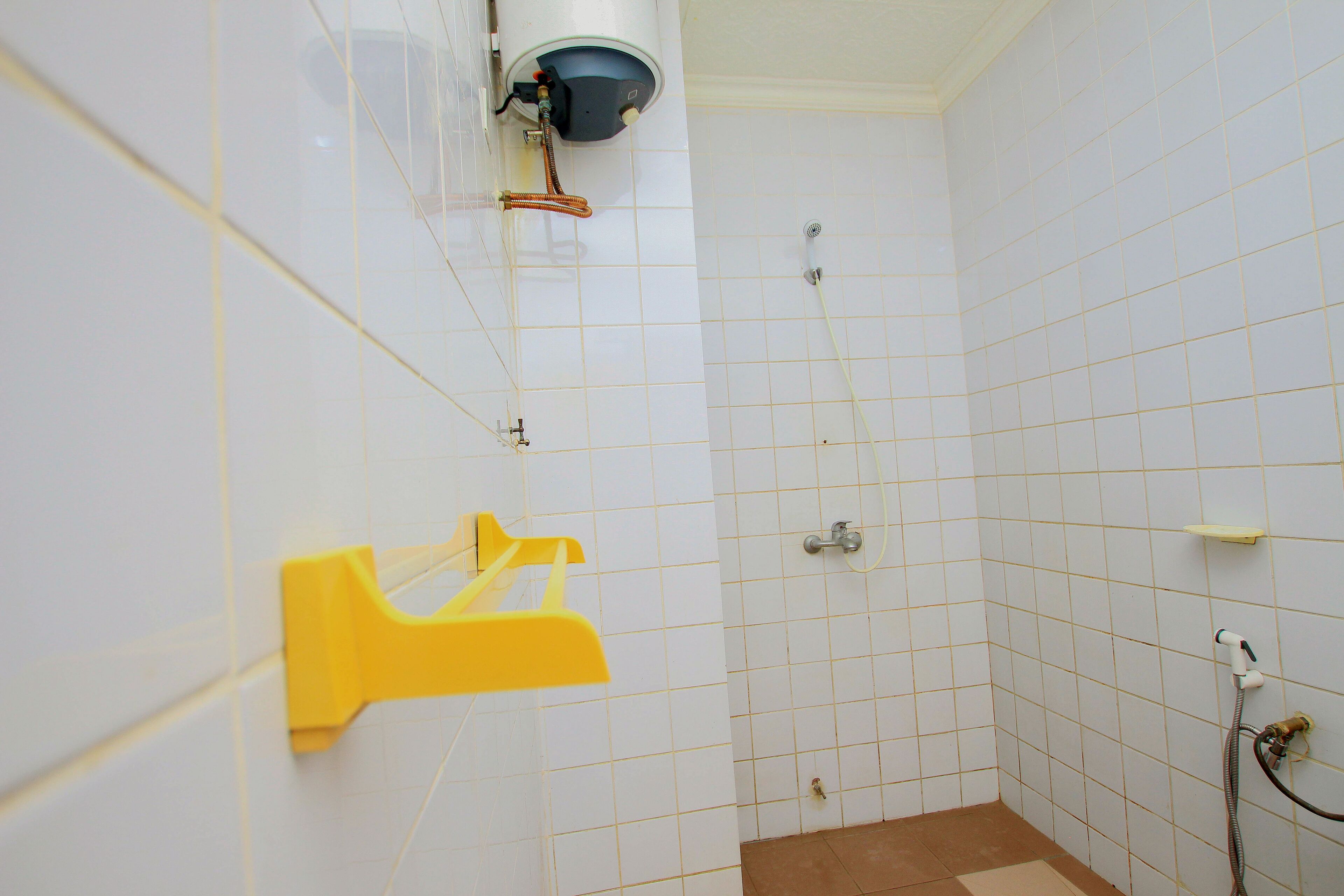 Un baño pequeño con azulejos, una ducha, un perchero amarillo y un calentador de agua instalado en la pared.