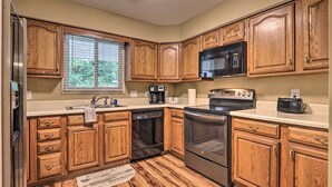 Una cocina con armarios de madera, un refrigerador de acero inoxidable, un microondas, una cafetera y un horno.