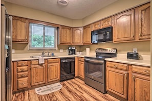 A kitchen with wooden cabinets, a stainless steel refrigerator, a microwave, a coffee maker, and an oven. - 1 Mi to Parkway! Flat-Access Pigeon Forge Condo (Pigeon Forge)