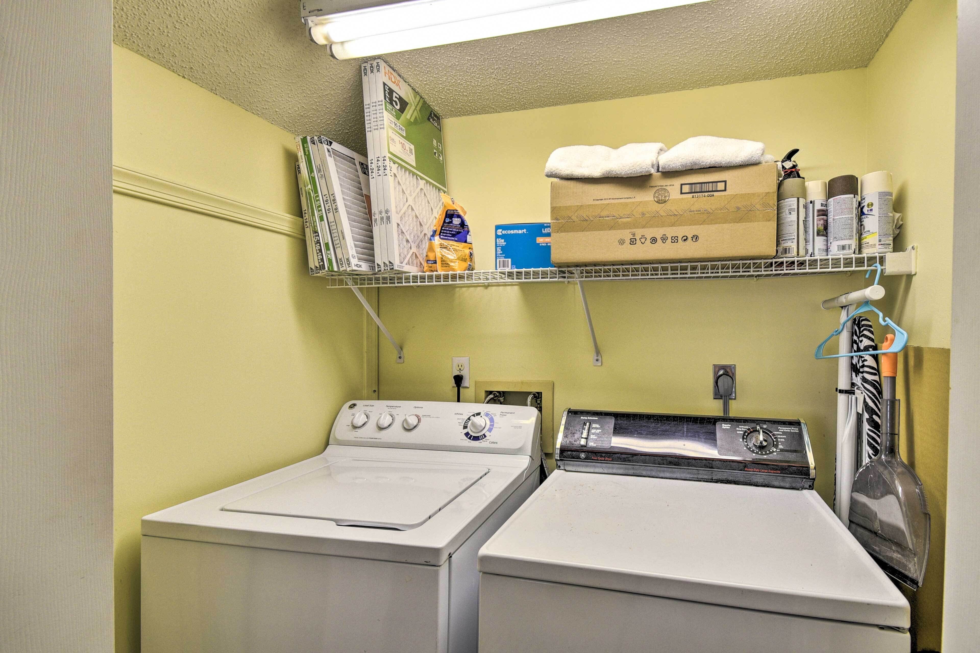 A laundry room with a washing machine, dryer, shelves with cleaning supplies, and a hanging rack.