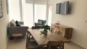 Ein modernes Wohnzimmer mit einem Holzesstisch, zwei Stühlen, einer Couch und einem an der Wand befestigten Fernseher.
