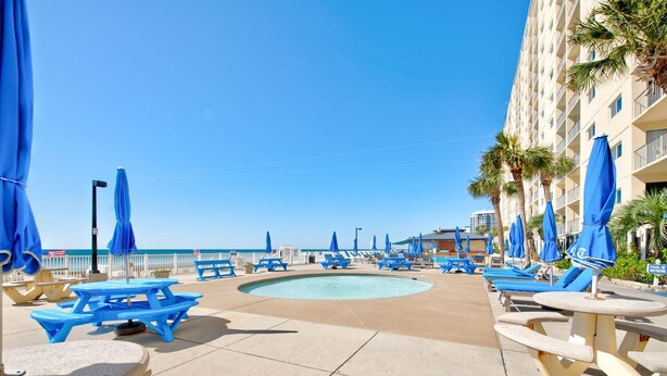 A pool area with blue lounge chairs and umbrellas, a small pool, and a building with balconies. - Make memories on the beach! Clean 3bd/2bth condo! (Panama City Beach)