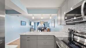 A modern kitchen with grey cabinets, a large island, stainless steel appliances, and a blue accent wall. - Make memories on the beach! Clean 3bd/2bth condo! (Panama City Beach)