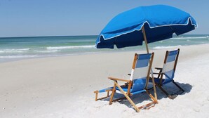 A beach with two wooden beach chairs and a blue umbrella. - Make memories on the beach! Clean 3bd/2bth condo! (Panama City Beach)