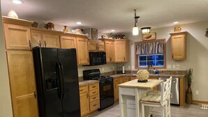 A kitchen with wooden cabinets, a black refrigerator, a microwave, a stove, and a small island with chairs.