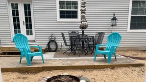 A backyard with two turquoise Adirondack chairs, a fire pit, and a wooden table with chairs.