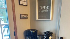 A coffee station with a coffee maker, espresso machine, and coffee cups on a wooden cabinet.