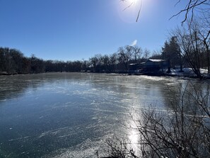 A frozen lake with a house on the right and bare trees in the background. - Cozy Chic Cabin on Private 10-acre Lake. (Independence)