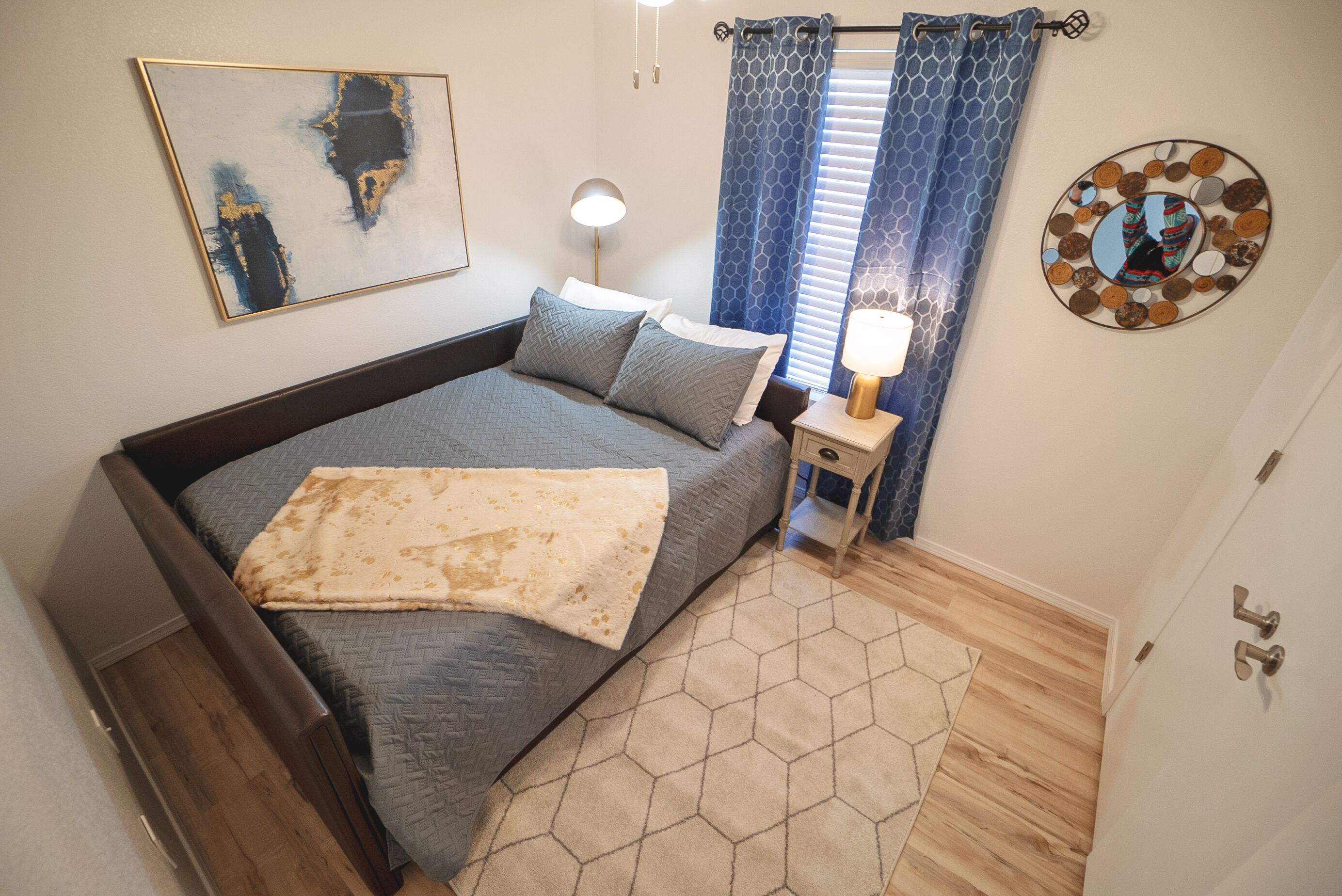 A neatly arranged bedroom with a bed, bedside table, lamp, and a decorative wall piece.