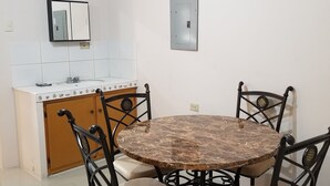 Zona pranzo con tavolo rotondo e quattro sedie, cucina con piastrelle bianche e un armadietto in legno, e una presa di corrente a parete.