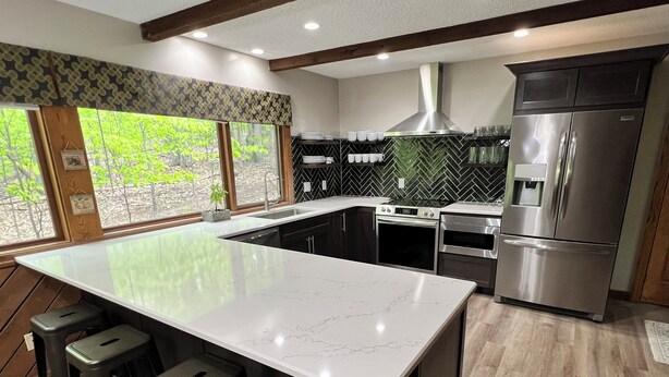 Uma cozinha moderna com uma ilha grande, banquetas, uma geladeira de aço inoxidável e um revestimento de parede em padrão herringbone.
