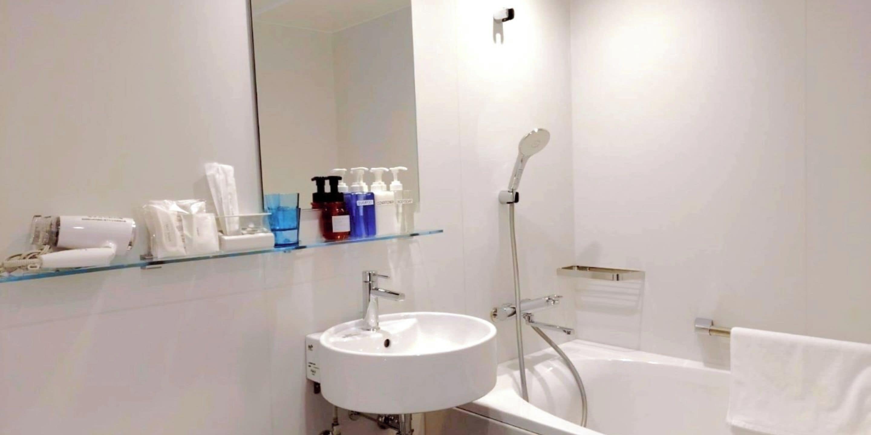 Uma casa de banho moderna com uma prateleira de vidro com artigos de higiene pessoal, uma pia branca e uma banheira.