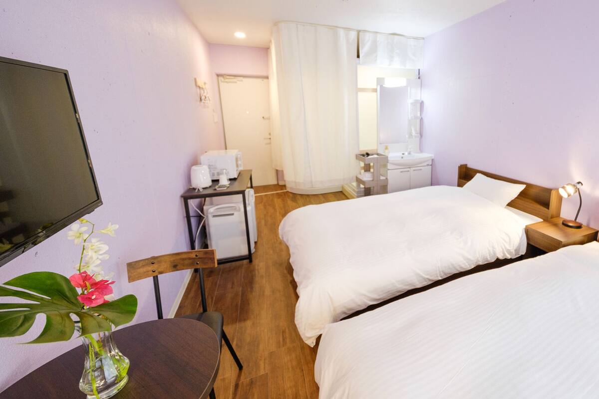 A hotel room with two beds, a desk, a chair, a TV, a bathroom, and a shower curtain.