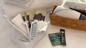 Et pænt arrangeret badeværelse med en stabel hvide håndklæder, en kurv med toiletartikler og en pakke japansk te.