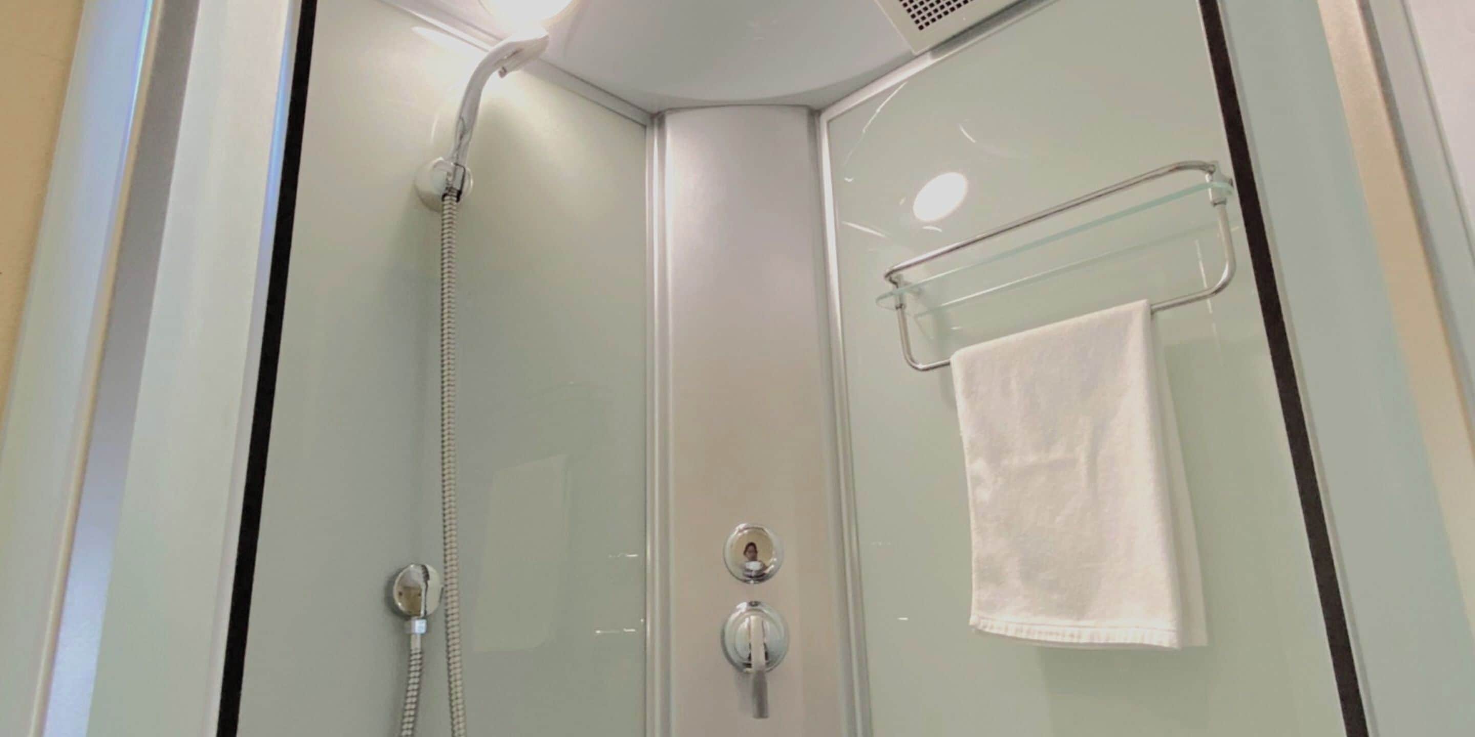 Ducha envuelta en vidrio con cabezal de ducha manual y un perchero para toallas.