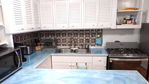 A kitchen with white cabinets, a blue countertop, a stainless steel sink, a microwave, a gas stove, and a patterned backsplash. - Hidden by beautiful palm and flamboyant trees but close to restaurants & stores  (Christiansted)