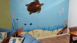 A room with a blue sofa, a wooden chair, and a wall mural depicting an underwater scene with a turtle. - Hidden by beautiful palm and flamboyant trees but close to restaurants & stores  (Christiansted)