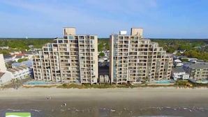 Un hotel sulla spiaggia con diversi edifici alti, una spiaggia sabbiosa e una vista limpida sull'oceano.