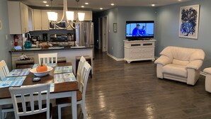 A modern kitchen with stainless steel appliances, a dining area with a wooden table and chairs, a white sofa, and a flat-screen TV. - Luxury beach house   (Seaside Heights)
