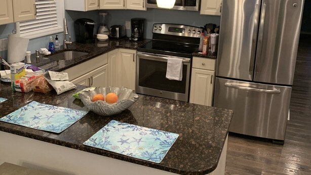 A modern kitchen with white cabinets, a stainless steel refrigerator, a microwave, and a gas stove. There are two bar stools and a granite countertop. - Luxury beach house   (Seaside Heights)