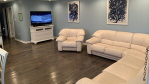 A living room with a sectional sofa, two armchairs, a TV on a white cabinet, and artwork on the walls. - Luxury beach house   (Seaside Heights)