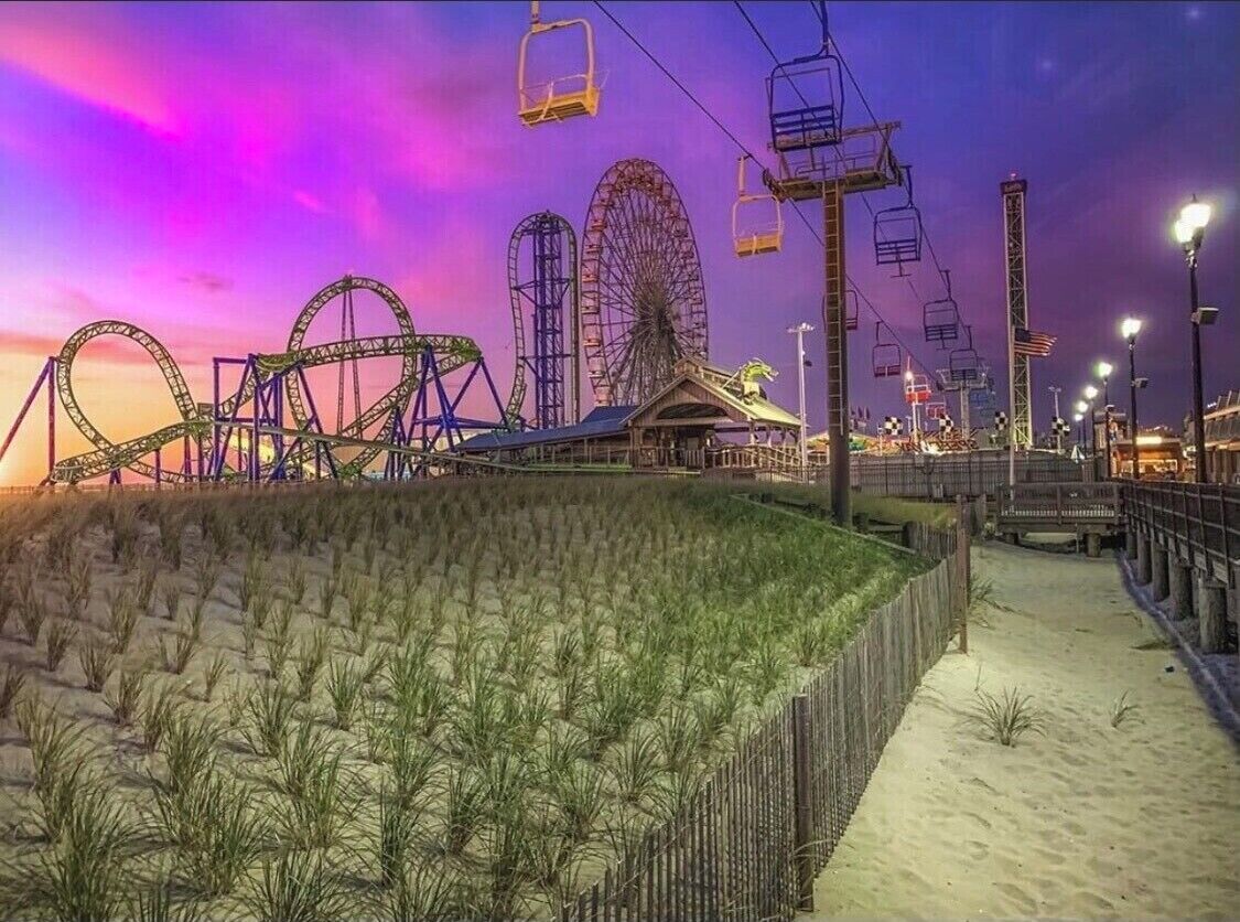 A beachside amusement park at dusk with roller coasters and a Ferris wheel.