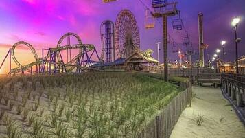A beachside amusement park at dusk with roller coasters and a Ferris wheel.