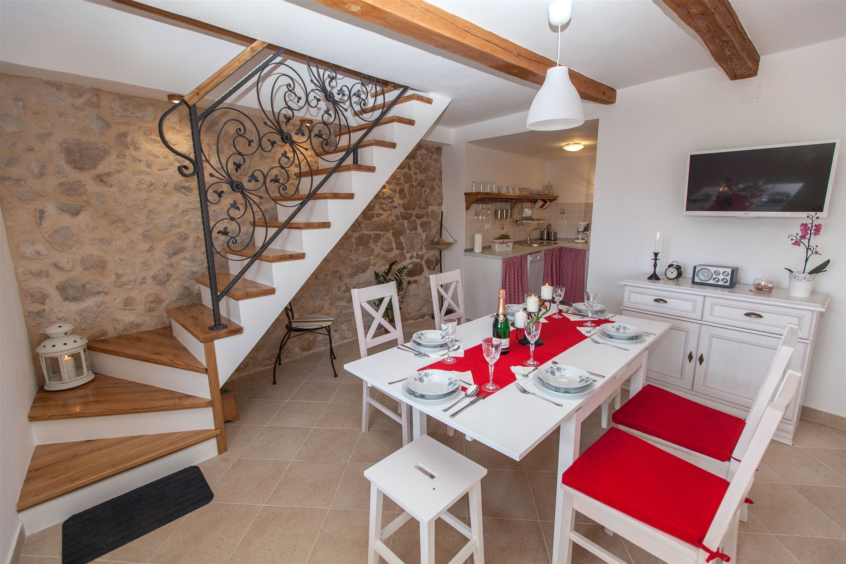 A dining area with a wooden staircase, stone wall, and a kitchen in the background.