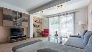 A modern living room with a large grey sofa, a flat-screen TV, a red chair, and a small table with a decorative bowl. - Villa Marta (Grizane)
