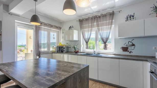 A modern kitchen with a wooden island, white cabinets, and a large window with curtains. - Villa Marta (Grizane)