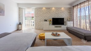 A modern living room with a sofa, a coffee table with croissants, a TV, and a stone wall. - Villa Marta (Grizane)