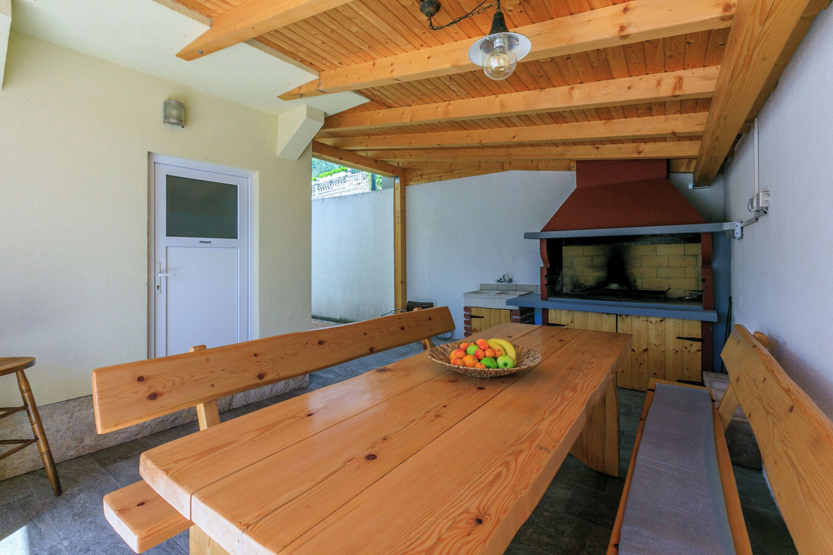 Een houten eettafel met banken, een fruitmand en een bakoven in een landelijke keuken.