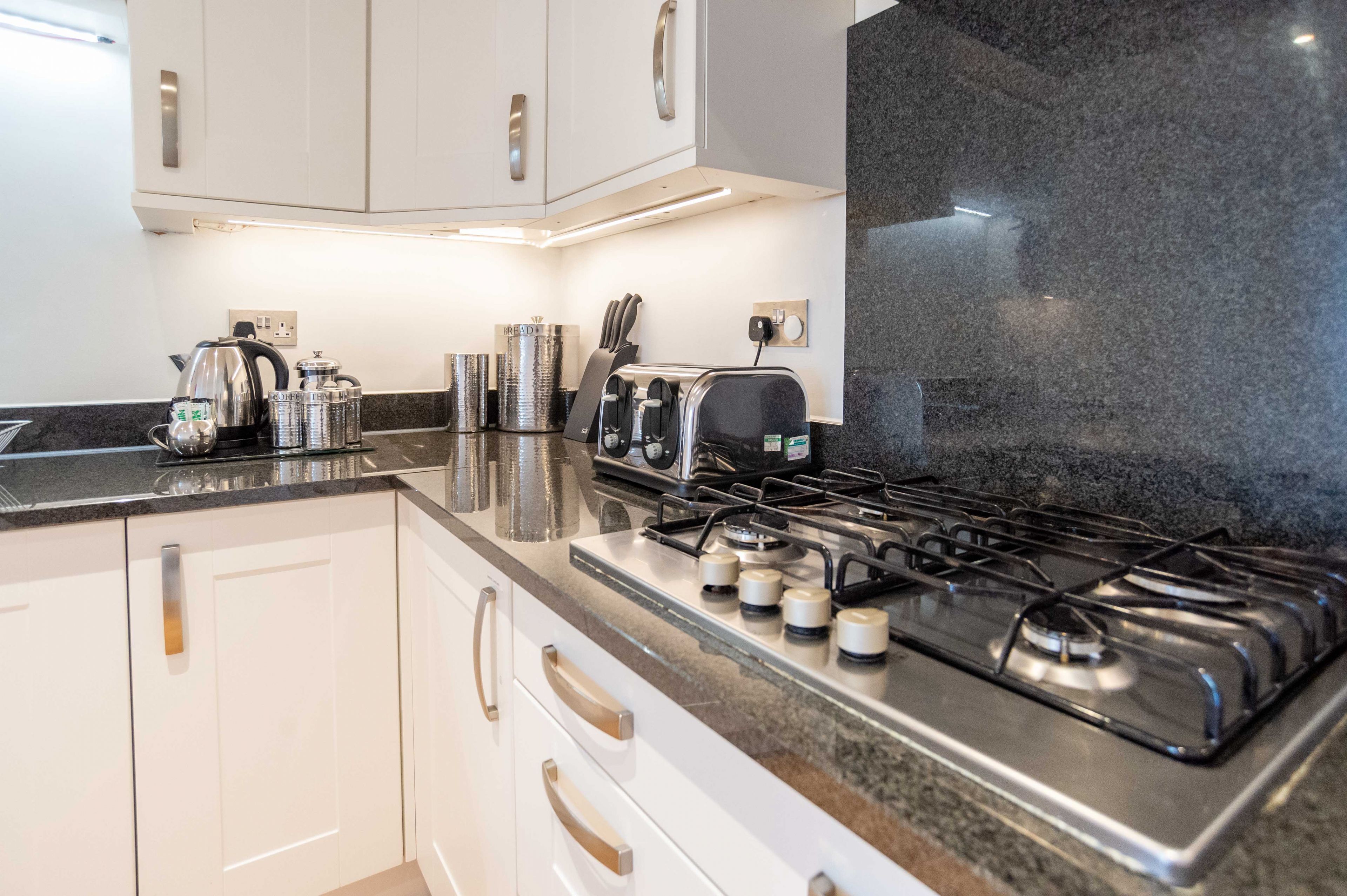 A modern kitchen with white cabinets, a granite countertop, a gas stove, a toaster, and a kettle.