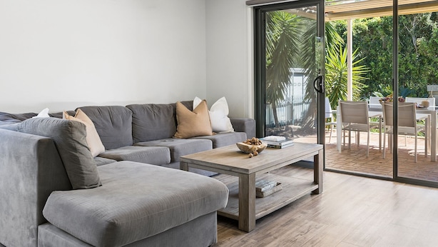 Ein modernes Wohnzimmer mit einem grauen Ecksofa, einem Holztisch und einer Schiebetür zu einem Außenbereich mit Terrasse.