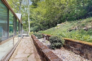 A stone pathway leading to a glass-enclosed structure, surrounded by lush greenery and a stone retaining wall.