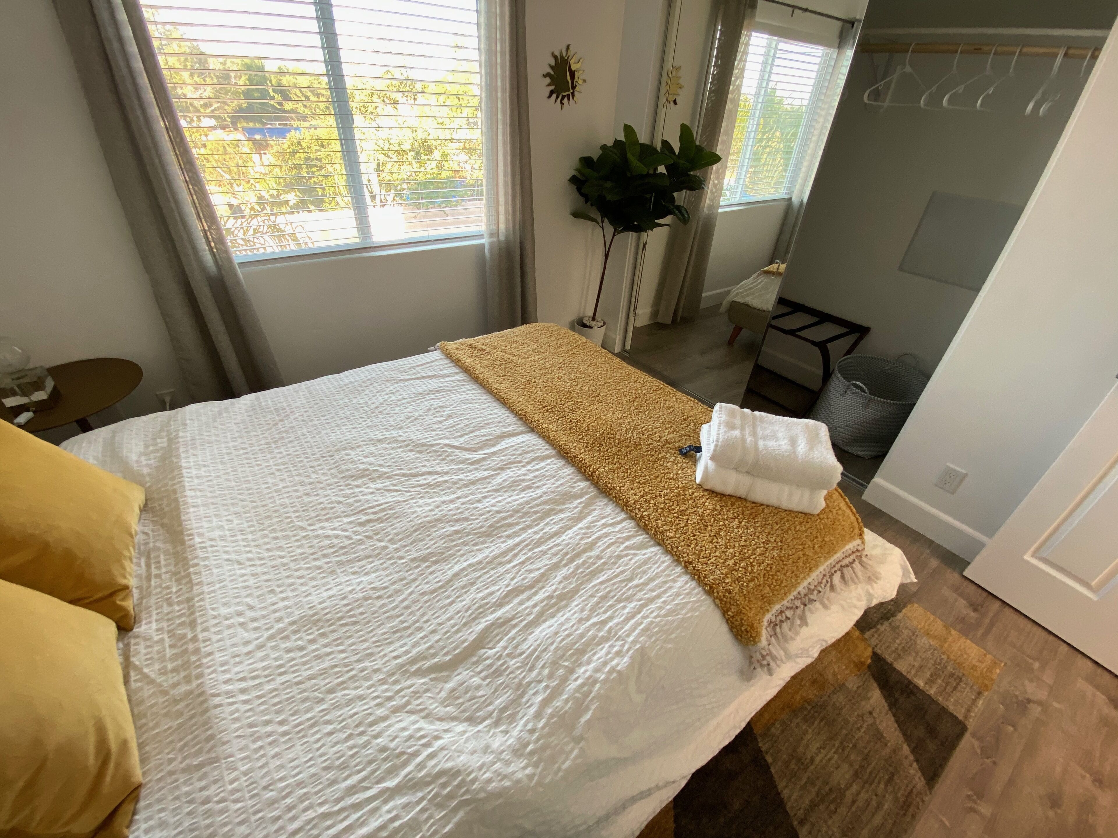 A neatly made bed with a white and beige blanket, a yellow pillow, and a folded white towel.