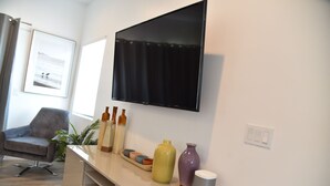 A living room with a flat-screen TV mounted on the wall, a grey armchair, a plant, and a console table with decorative vases and a small shelf. - *Cali King Bed * Bright Natural Light * Tall Ceilings * Full Kitchen * Balcony (San Diego)